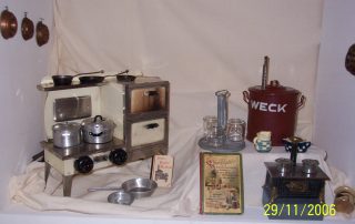 Historische Küchenutensilien mit Puppenherd und Einmachgläsern ausgestellt.
