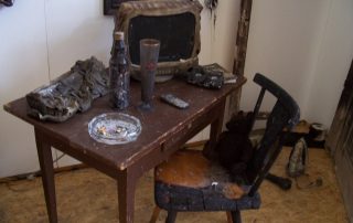 Verbrannter Tisch mit beschädigtem Stuhl, Flaschen und Gegenständen darauf.