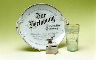 Dekoratives Geschirrset zur Verlobung, bestehend aus einem verzierten Teller mit der Aufschrift "Zur Verlobung", einem Trinkglas mit der Aufschrift "Zur Verlobung" .