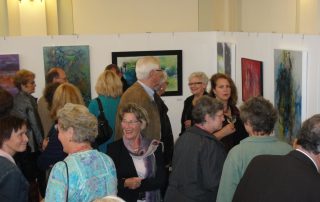 Besucher einer Ausstellung betrachten Gemälde und unterhalten sich angeregt.