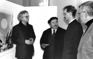 Vier Männern, die in einem Ausstellungsraum über ein abstraktes Kunstwerk sprechen.