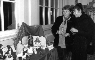 Zwei Frauen betrachten eine weihnachtliche Krippenausstellung mit Figuren, Tieren und einer dekorativen Kulisse.
