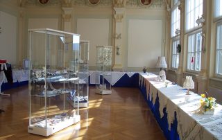 Ausstellung mit Vitrinen und Tischdecken in festlichem Ausstellungsraum.