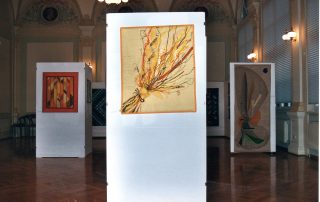 Alt-Text: Ausstellung im Gewerbemuseum Spaichingen mit kunstvollen Textilarbeiten, die auf weißen Stellwänden präsentiert werden.