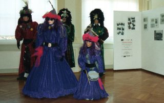 Ausstellung mit Figuren in farbenfrohen, glitzernden Fasnachtskostümen, darunter Masken und Hüte.